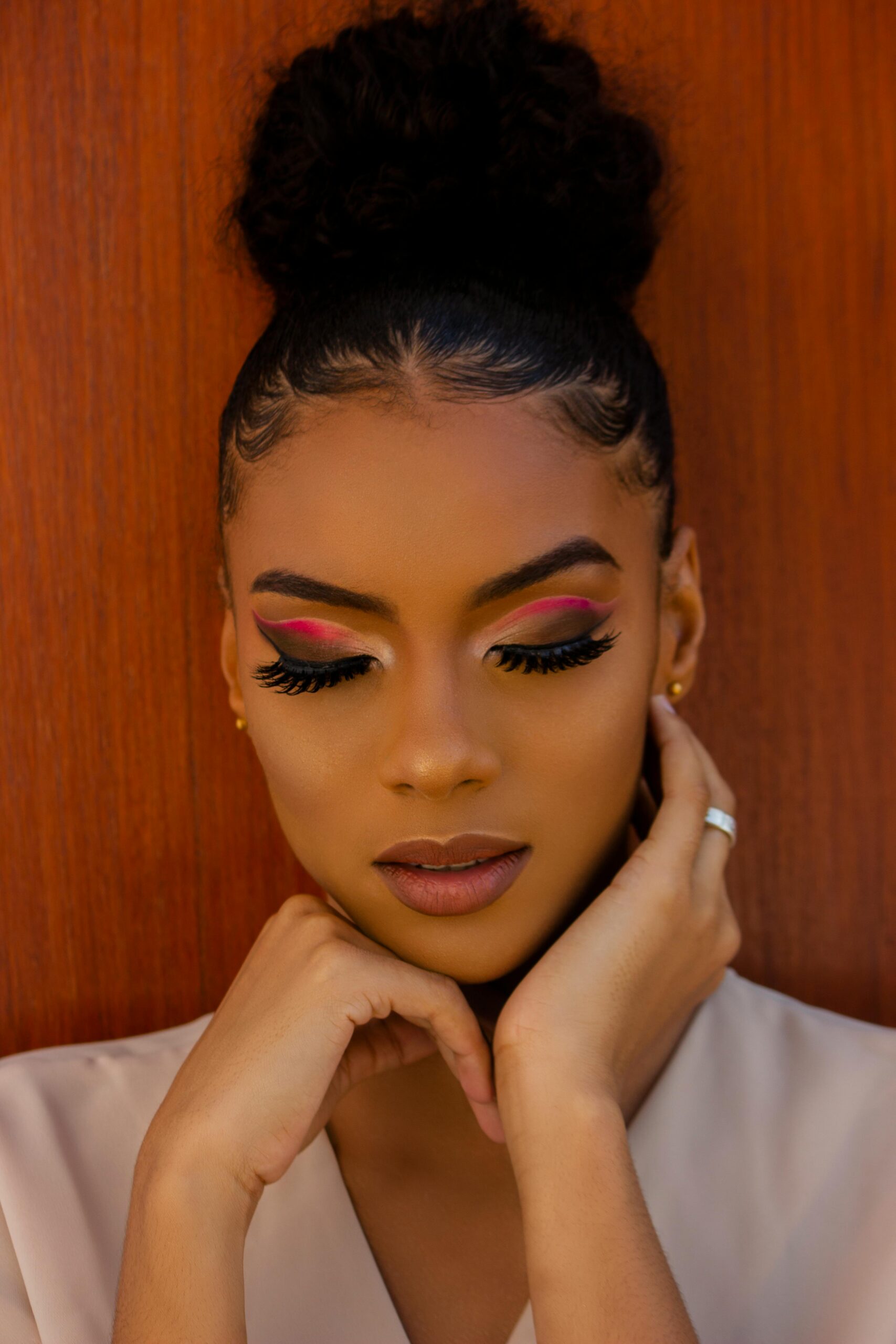 Close-up portrait of a woman with elegant hairstyle and vibrant eye makeup against a wooden background.