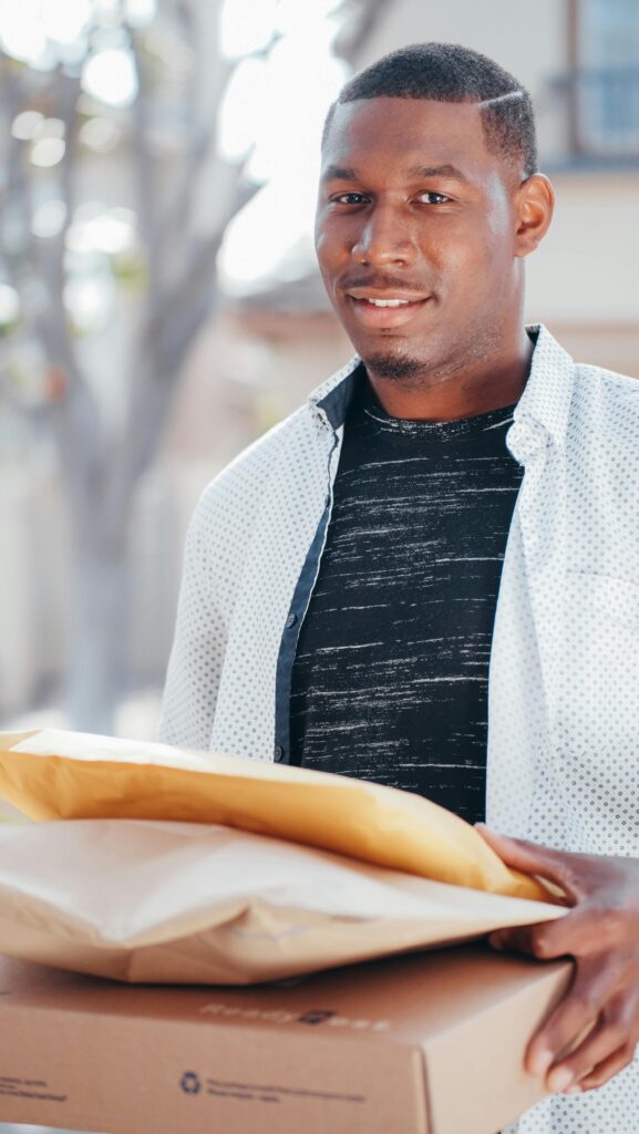 A deliveryman holding packages, ready for shipment, outdoors on a sunny day.